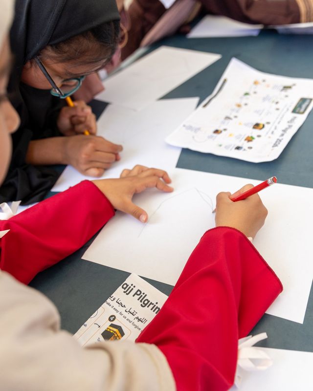 Children drawing at a table on our Hajj day, with a Hajj worksheet and coloured pencils beside them.