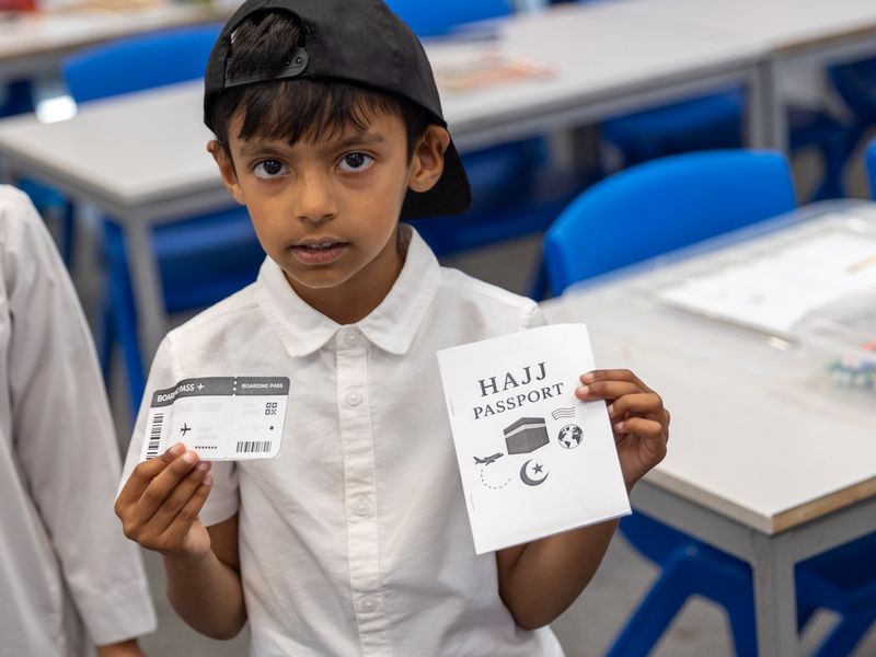 A boy holding up the Hajj passport and boarding pass he made on our Hajj day.