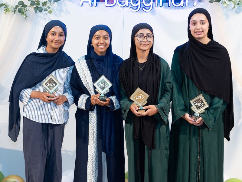 Four older students holding their awards in front of the Al Bayyinah sign.