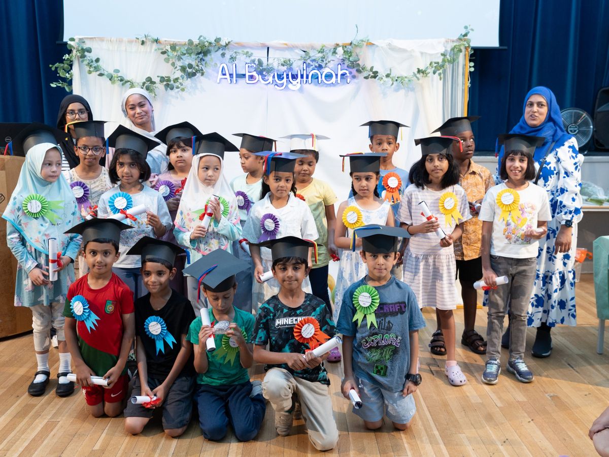 Early years graduates in mortarboards and rosettes, holding their scrolls, with their teachers.